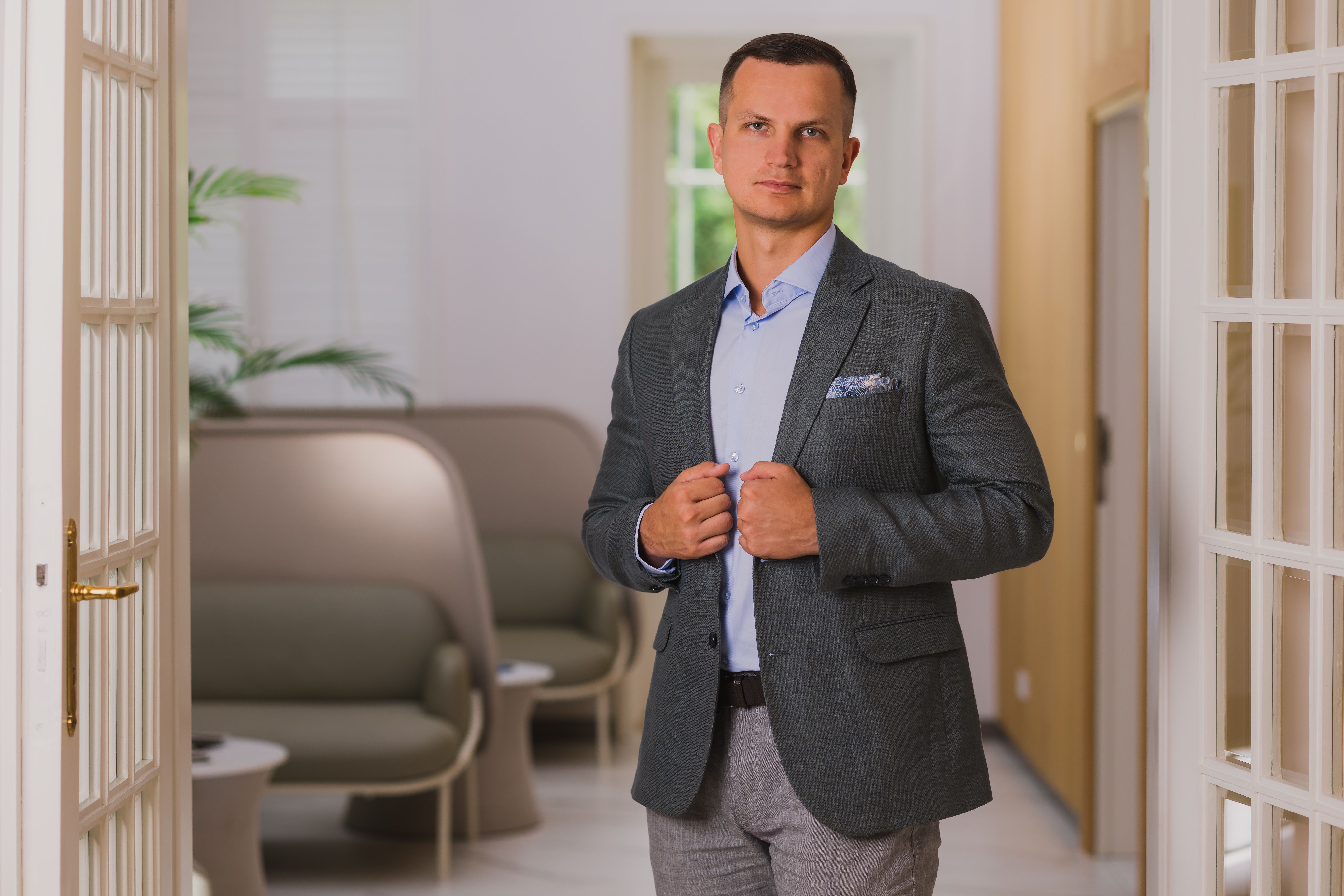 Mateusz Gładysz przy drzwiach francuskich, antracytowa marynarka, dłonie przy klapach